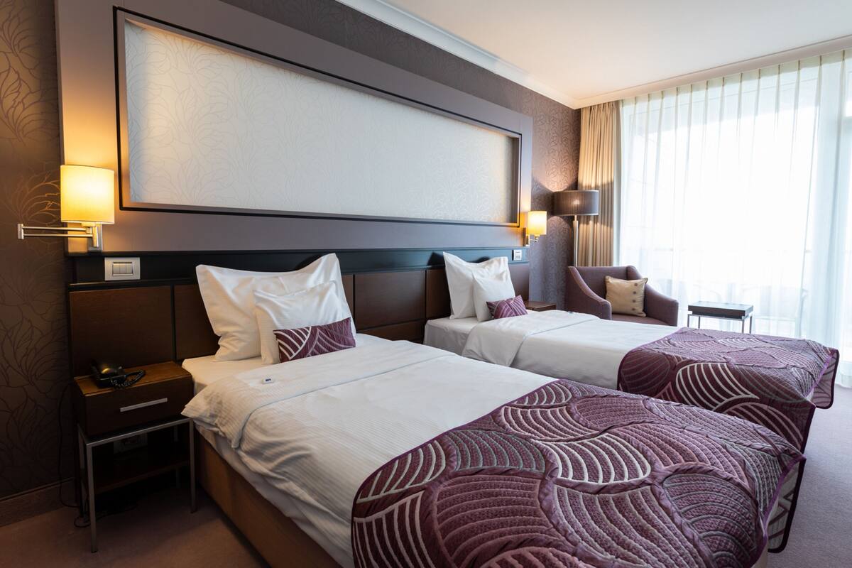 A hotel room with two beds, a large flat-screen TV, bedside lamps, a small table, and a chair.