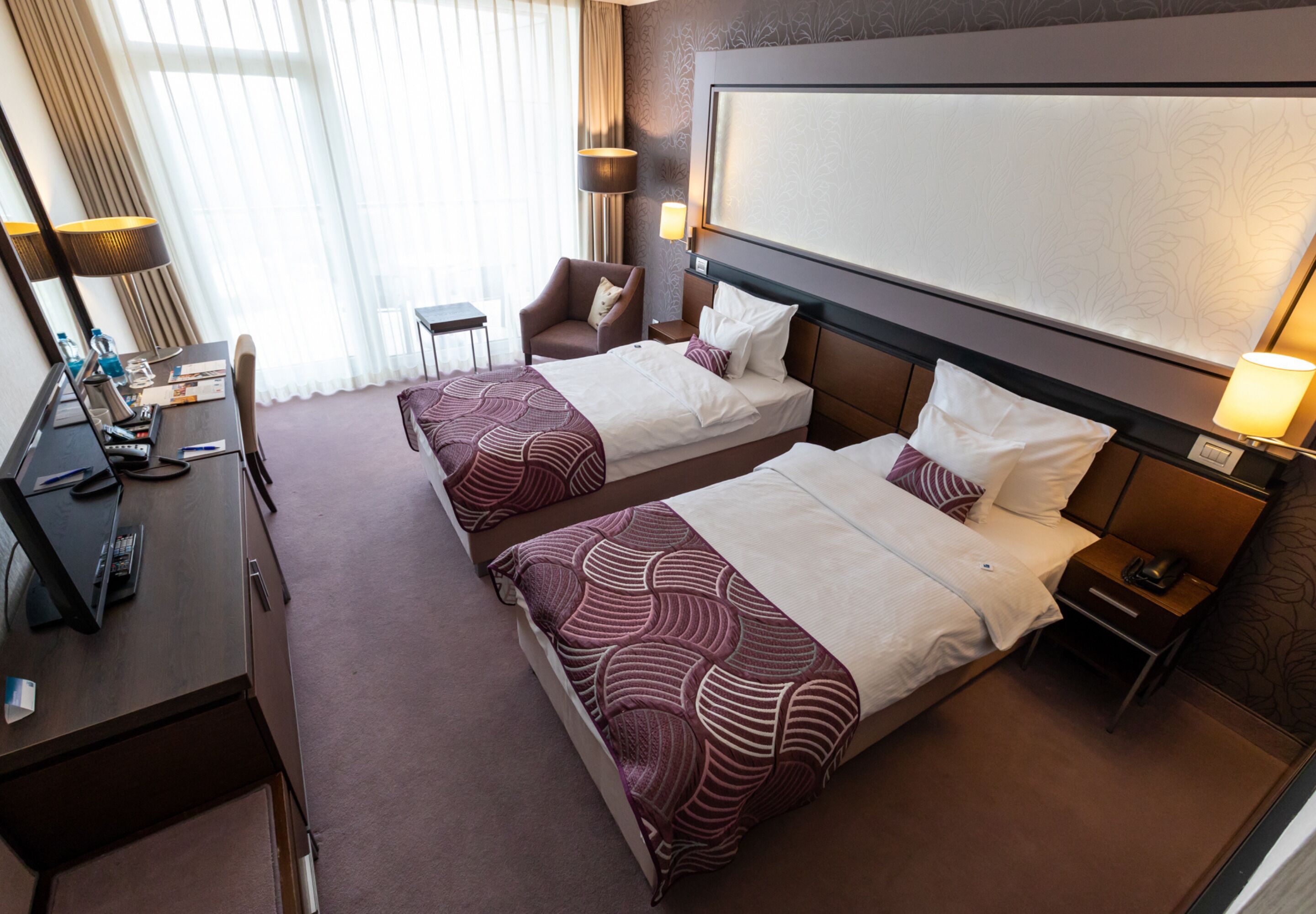 A hotel room with two beds, a desk with a computer, a chair, and a TV.