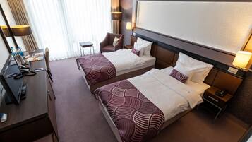 A hotel room with two beds, a desk with a computer, a chair, and a TV.