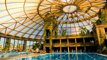 A large indoor swimming pool with a glass ceiling and multiple levels of balconies.