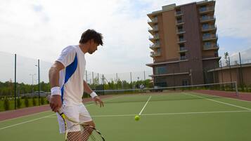 A tennis court with a net, a player in white and blue, and a building in the background.