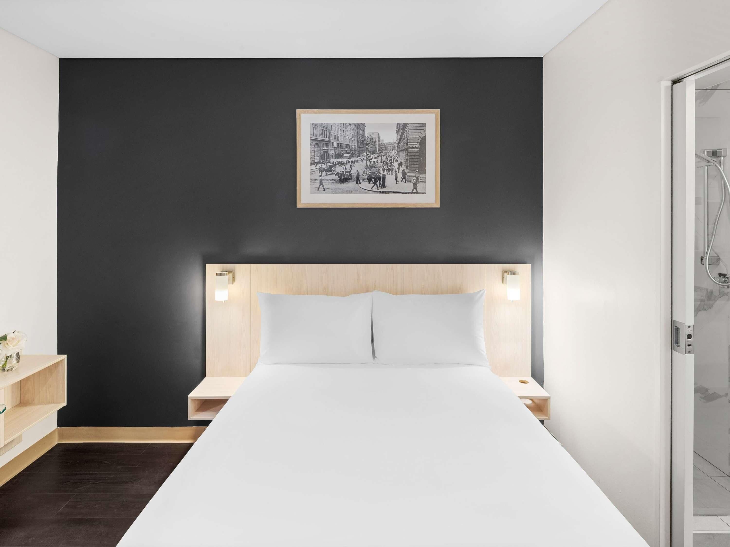Una habitación de hotel moderna con una cama grande, una pared de acento oscura, un cuadro enmarcado y una zona de ducha.