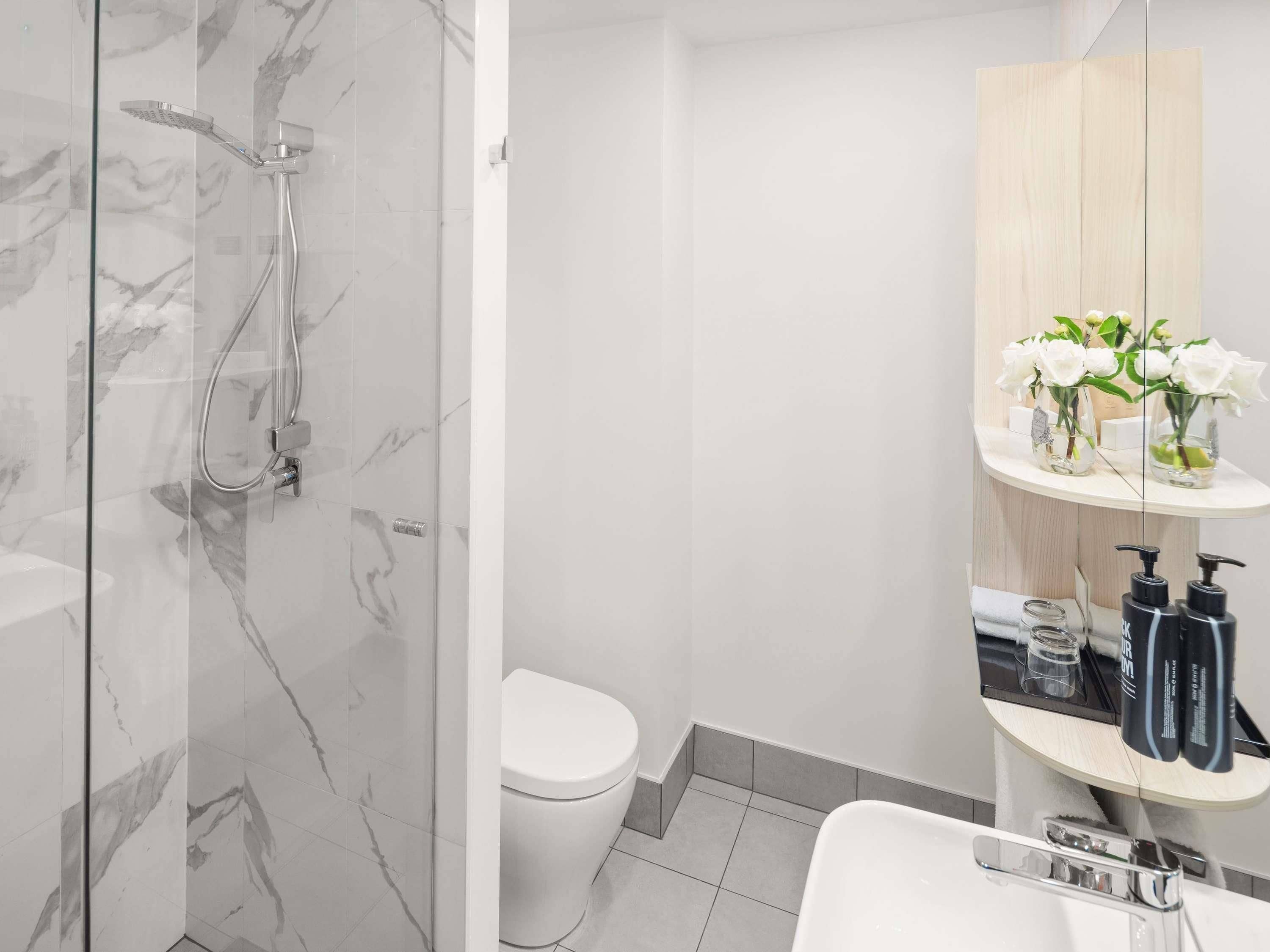 Un baño moderno con ducha envuelta en vidrio, inodoro blanco y tocador con espejo y artículos de aseo.
