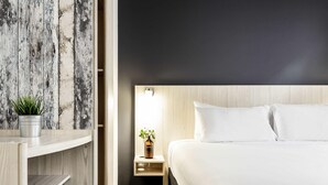 Una habitación de hotel moderna con una cama, una mesita de noche y una planta en maceta.
