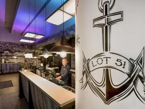 Un espace bar avec un comptoir, des luminaires suspendus et une fresque murale représentant un paysage urbain.