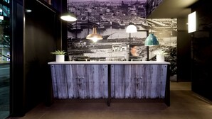 Un mostrador de recepción con un mural de la ciudad, iluminación colgante y una planta en maceta.