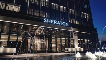 Un hotel con una fuente de agua en primer plano, un letrero que dice 'SHERATON' y una fachada de edificio moderna.