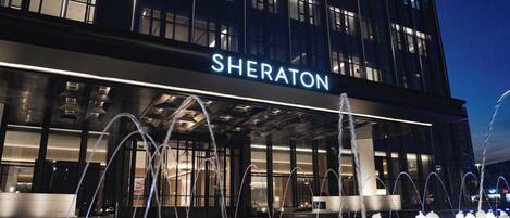 Un hotel con una fuente de agua en primer plano, un letrero que dice 'SHERATON' y una fachada de edificio moderna.