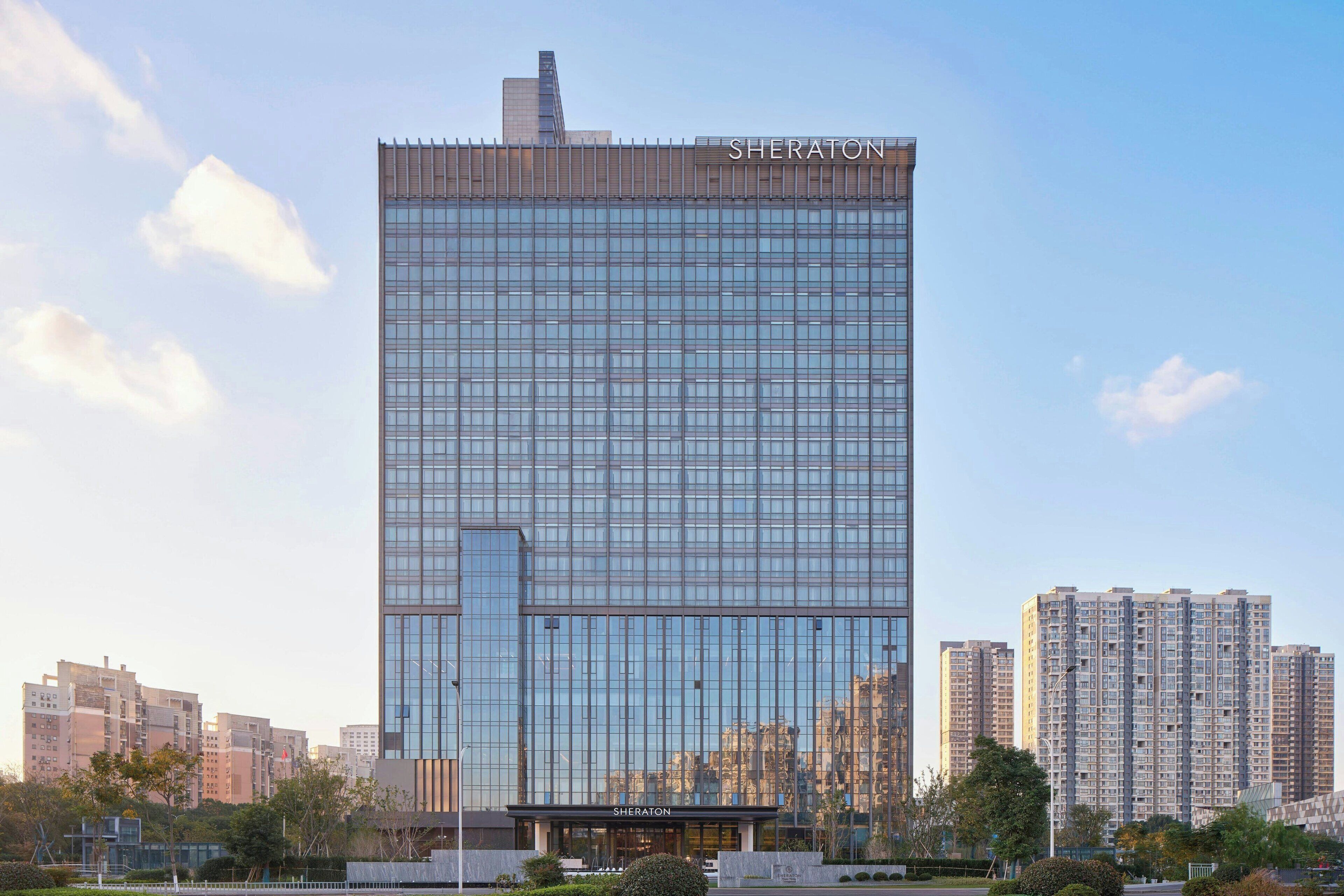 A modern Sheraton hotel with a glass facade, surrounded by high-rise buildings.