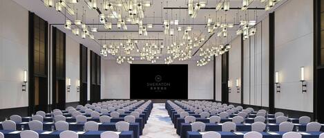 A conference room with rows of white chairs, a stage with a screen, and modern lighting fixtures.