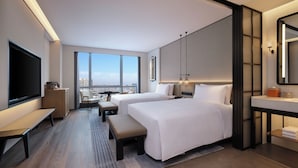 Una habitación de hotel moderna con dos camas, un televisor grande, un escritorio y vistas a la ciudad.