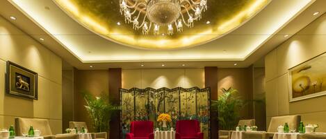 A luxurious hotel room with a large chandelier, a traditional Chinese screen, and a red sofa set.