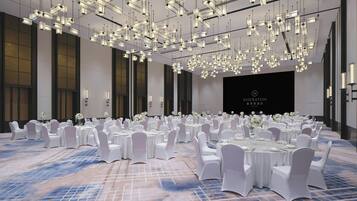 A banquet hall with round tables, white chairs, and hanging pendant lights.