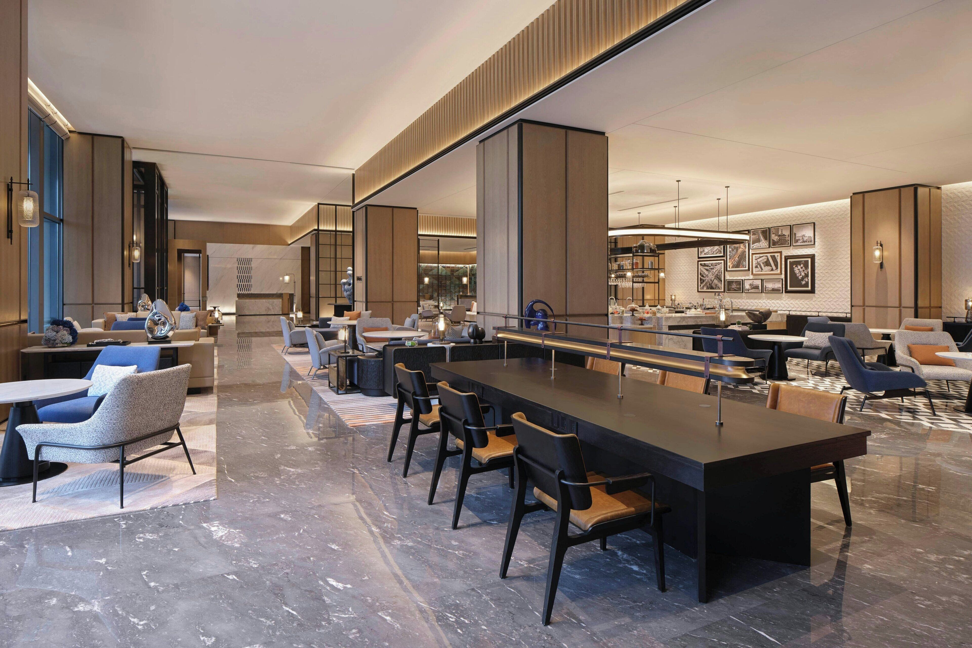 Eine moderne Hotelhalle mit langer Rezeption, einer Sitzecke mit Sesseln und Sofas sowie einer Bar.
