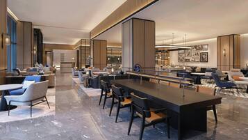 Eine moderne Hotelhalle mit langer Rezeption, einer Sitzecke mit Sesseln und Sofas sowie einer Bar.