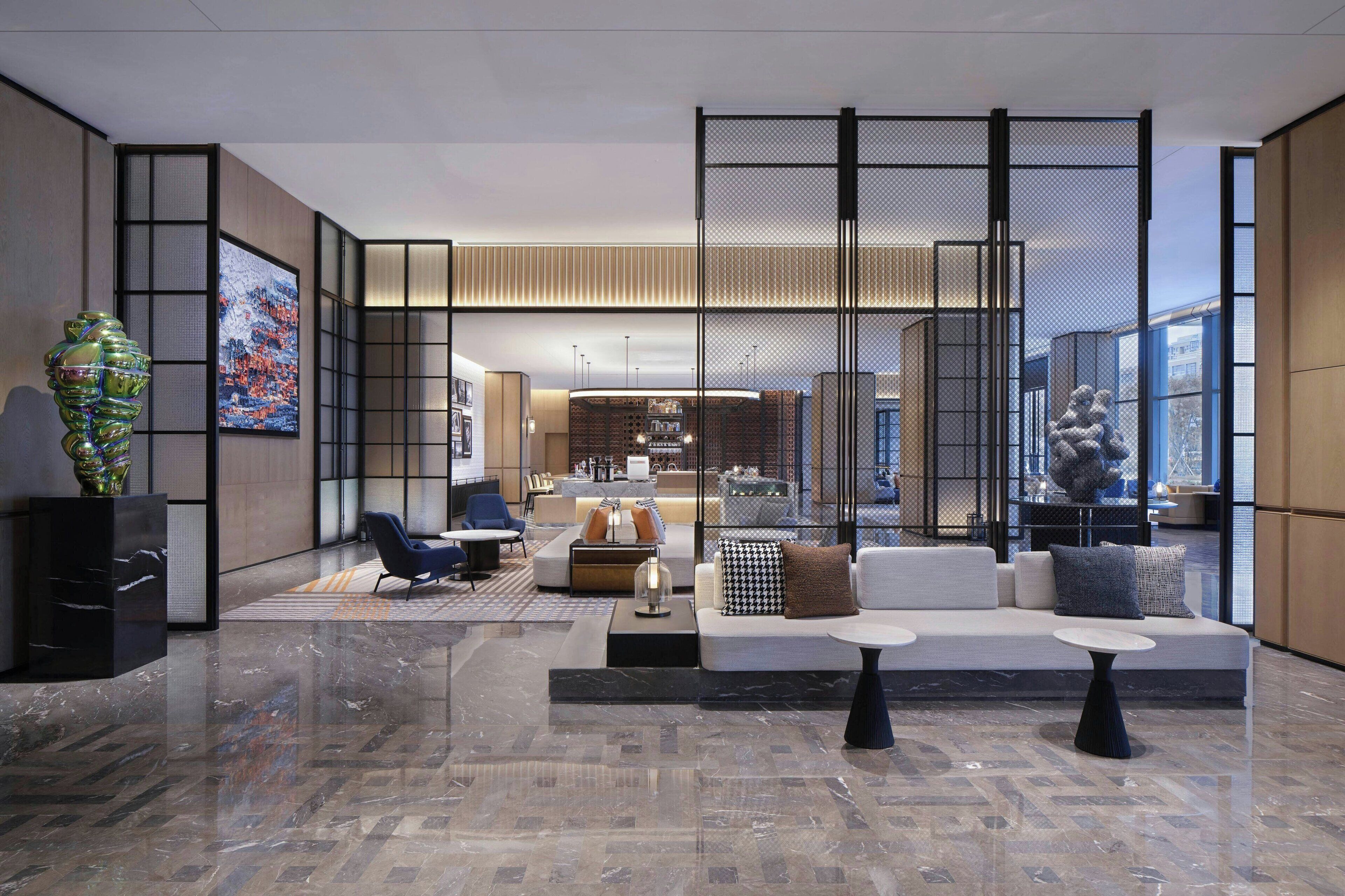 A modern lobby with a seating area, a reception desk, and a large window offering a view of the city.