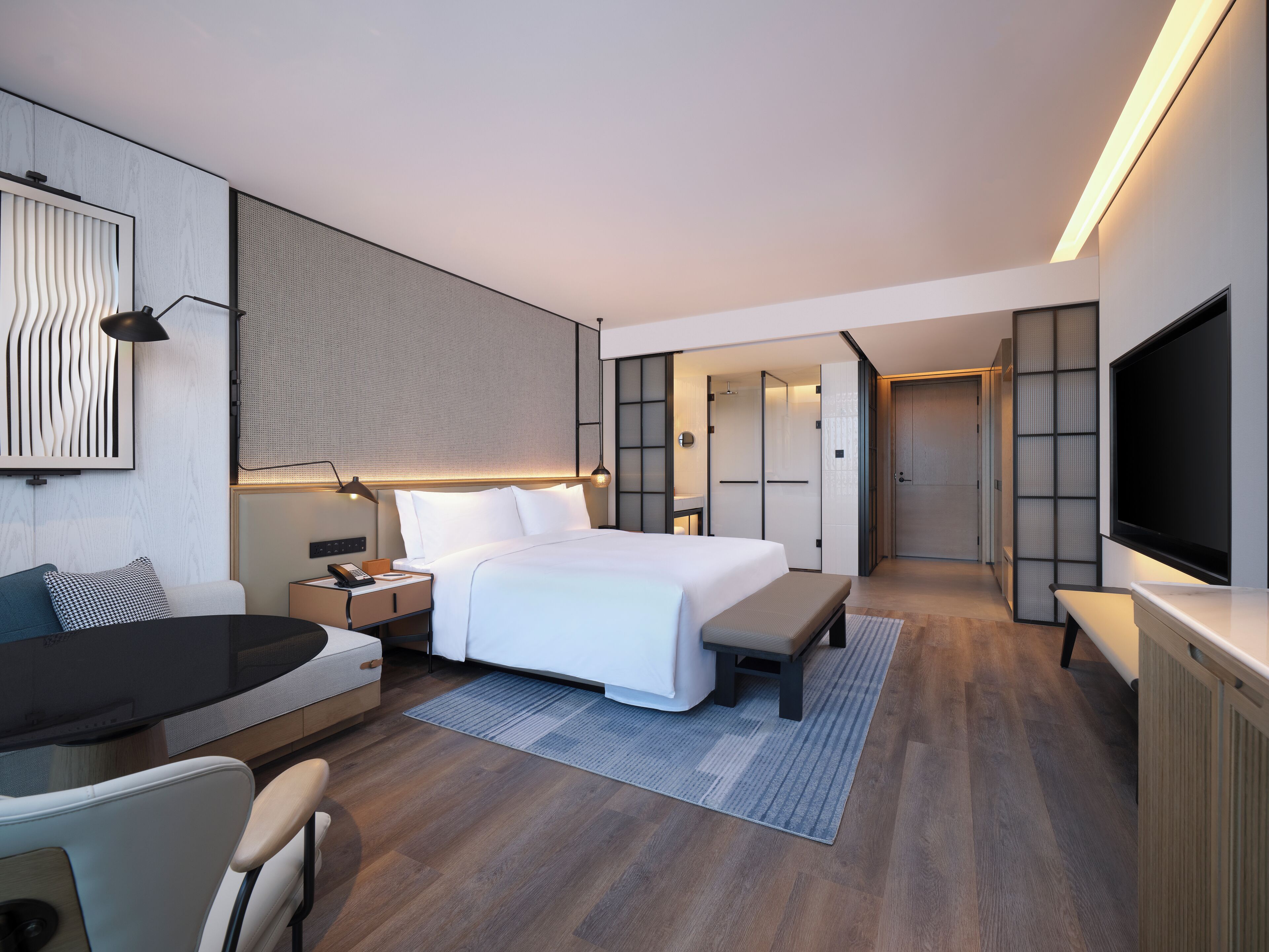 A modern hotel room with a large bed, a desk, a TV, and a walk-in closet.