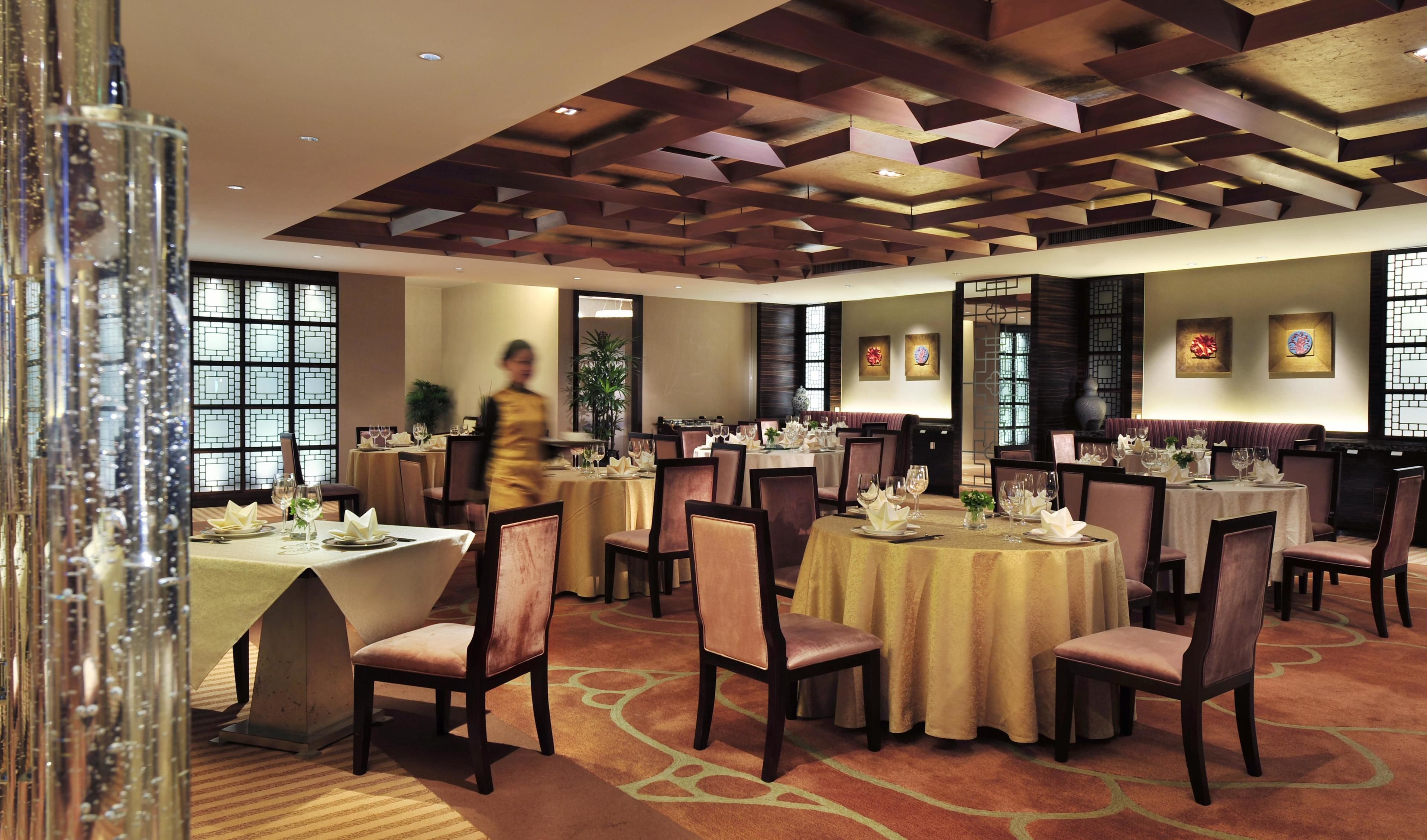 Comedor de hotel con varias mesas redondas dispuestas para los huéspedes, con un diseño de techo moderno y elementos decorativos tradicionales.