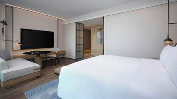 Quarto de hotel moderno com uma cama grande, televisão de tela plana, escrivaninha com cadeira e um pequeno espaço para sentar.