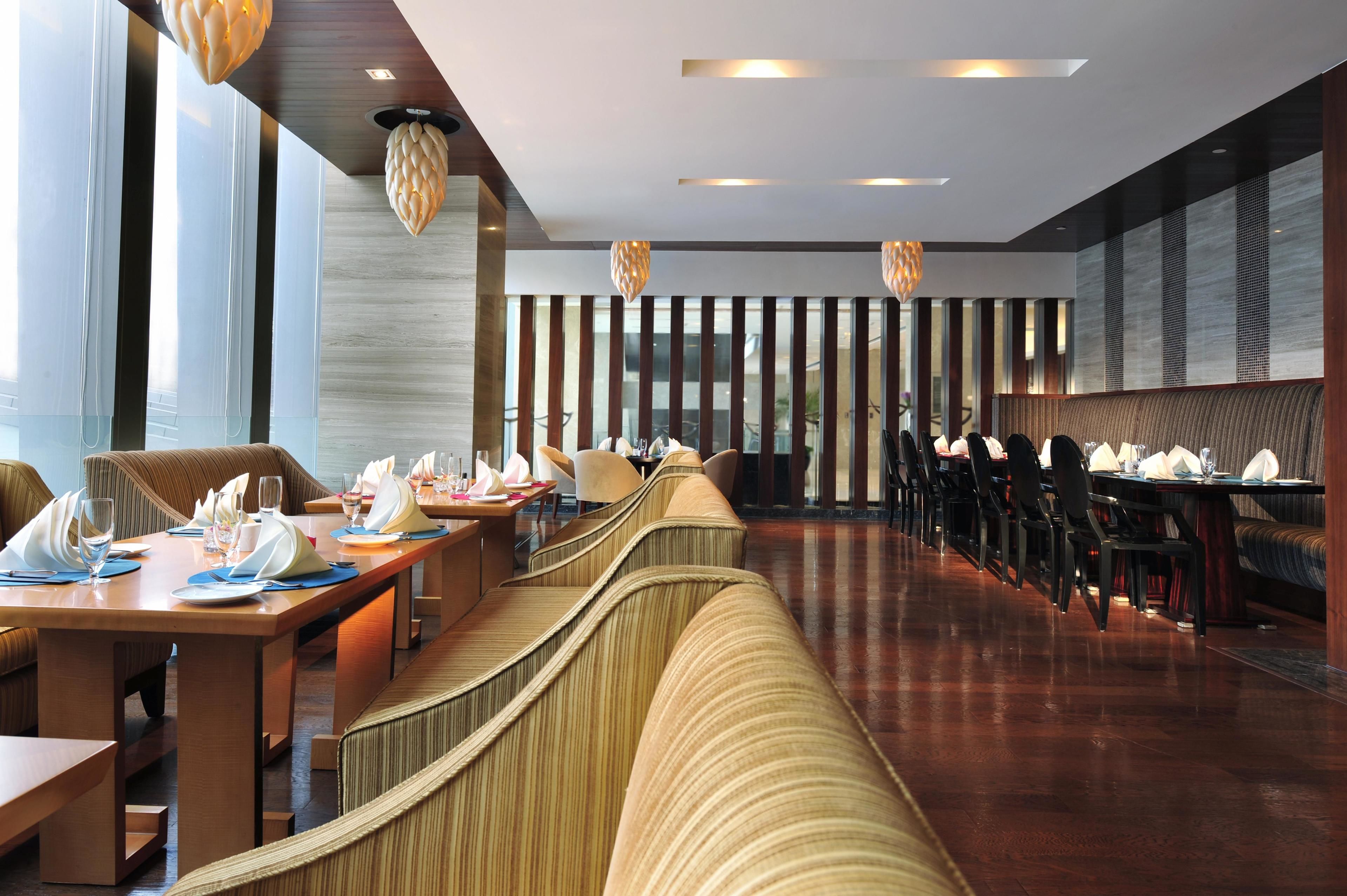Un restaurante moderno con mesas compartidas largas, asientos acolchados e iluminación colgante.