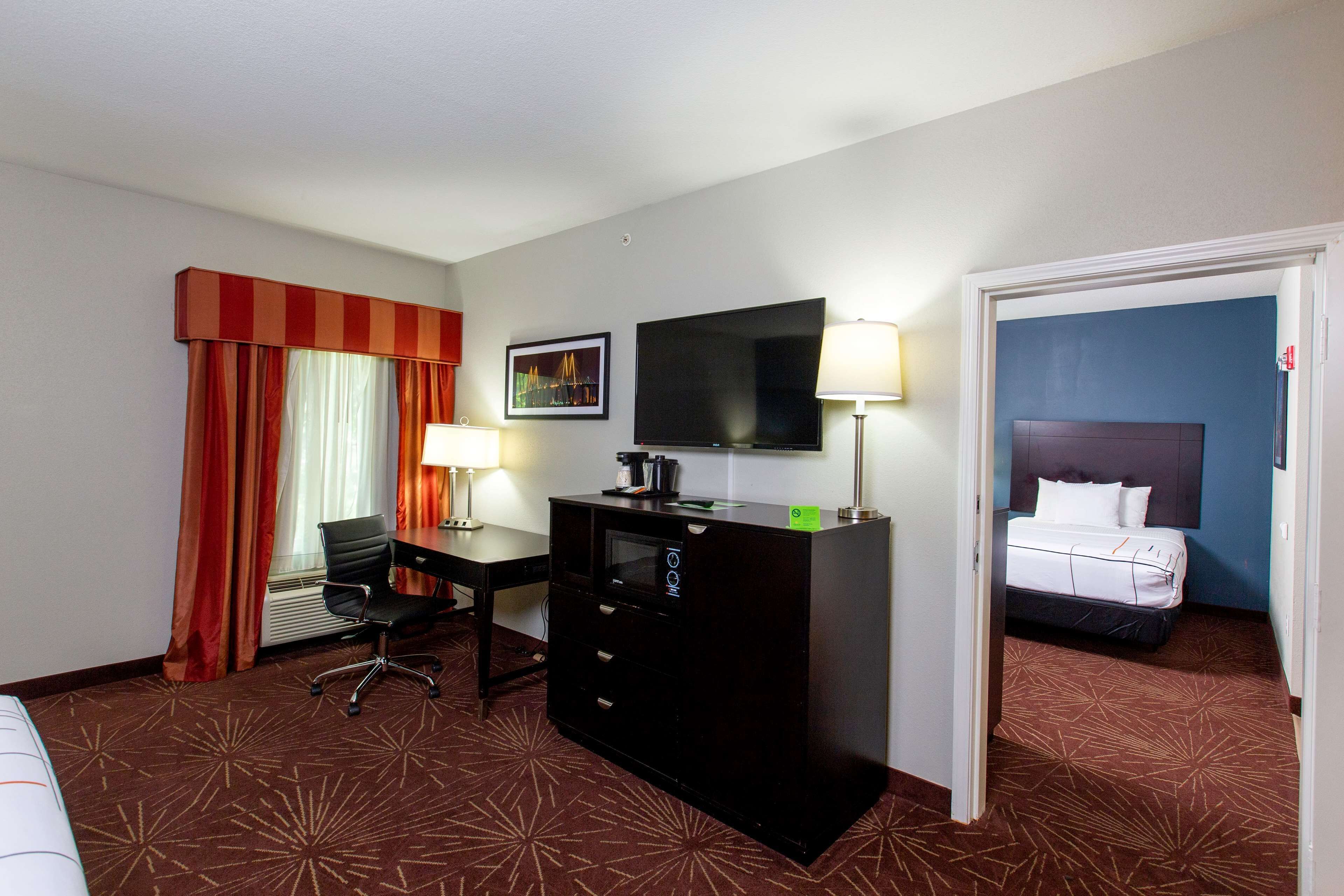 A hotel room with a bed, a desk with a chair, a TV, and a minibar.