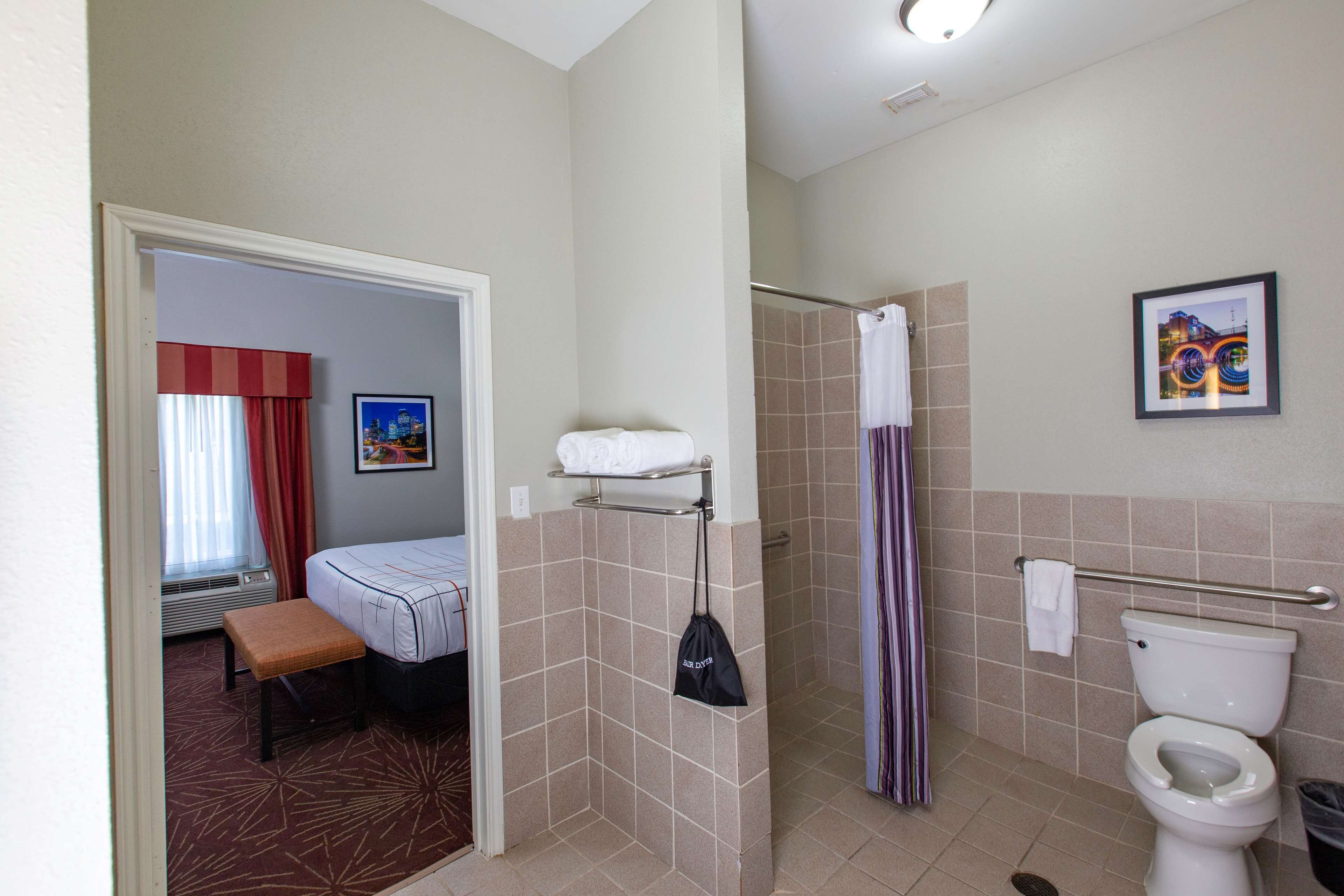 Un baño de hotel con ducha, inodoro y una cama con un banco.