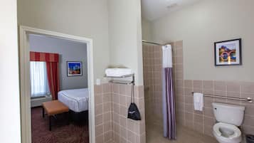 Un baño de hotel con ducha, inodoro y una cama con un banco.