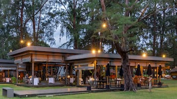 An outdoor restaurant with a covered seating area, surrounded by trees.