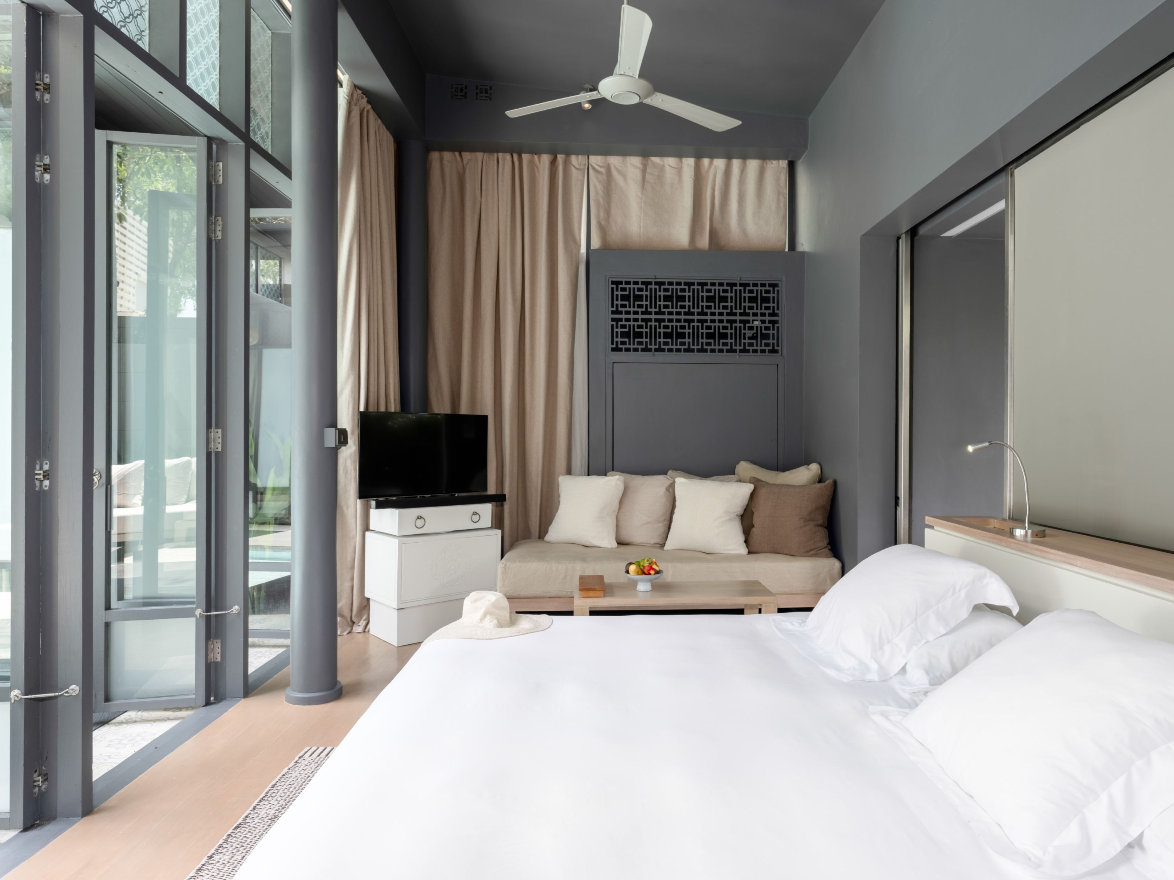 A modern hotel room with a bed, a sofa, a television, and a large window.