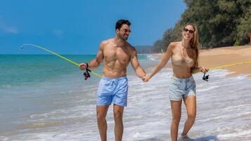 Una pareja sosteniendo cañas de pescar en una playa con cielos despejados y agua tranquila.