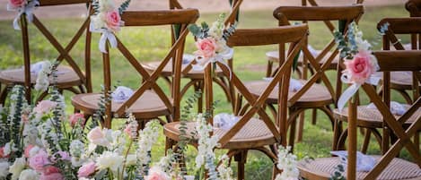 Outdoor wooden chairs arranged in rows, likely for an event, with floral decorations.