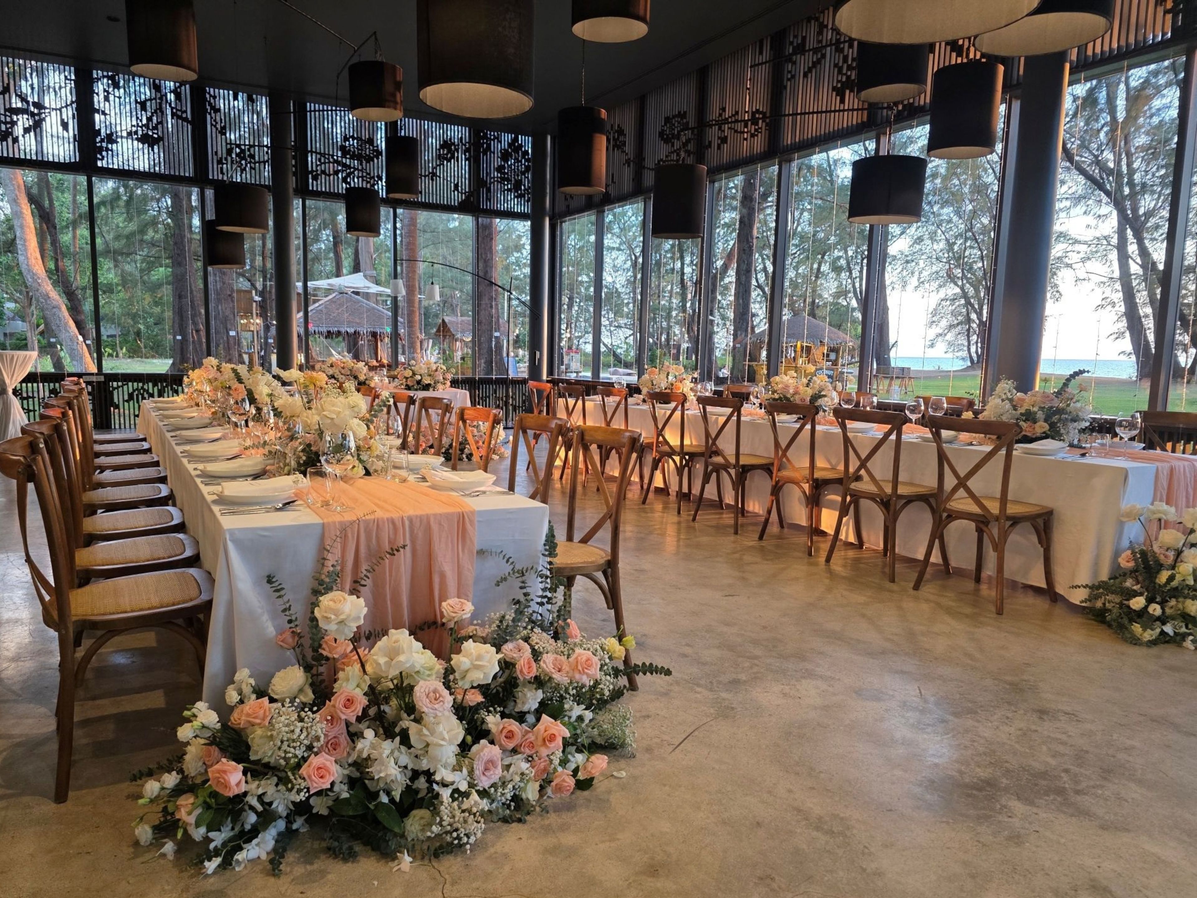 A long dining table with chairs, surrounded by large windows with a view of trees.