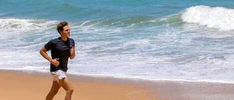 Une personne court sur une plage de sable, avec les vagues de l’océan en arrière-plan.