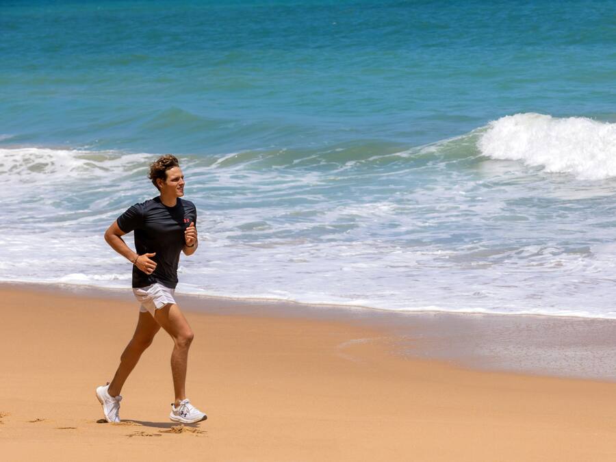 Una persona corriendo sobre una playa arenosa con olas del océano al fondo.