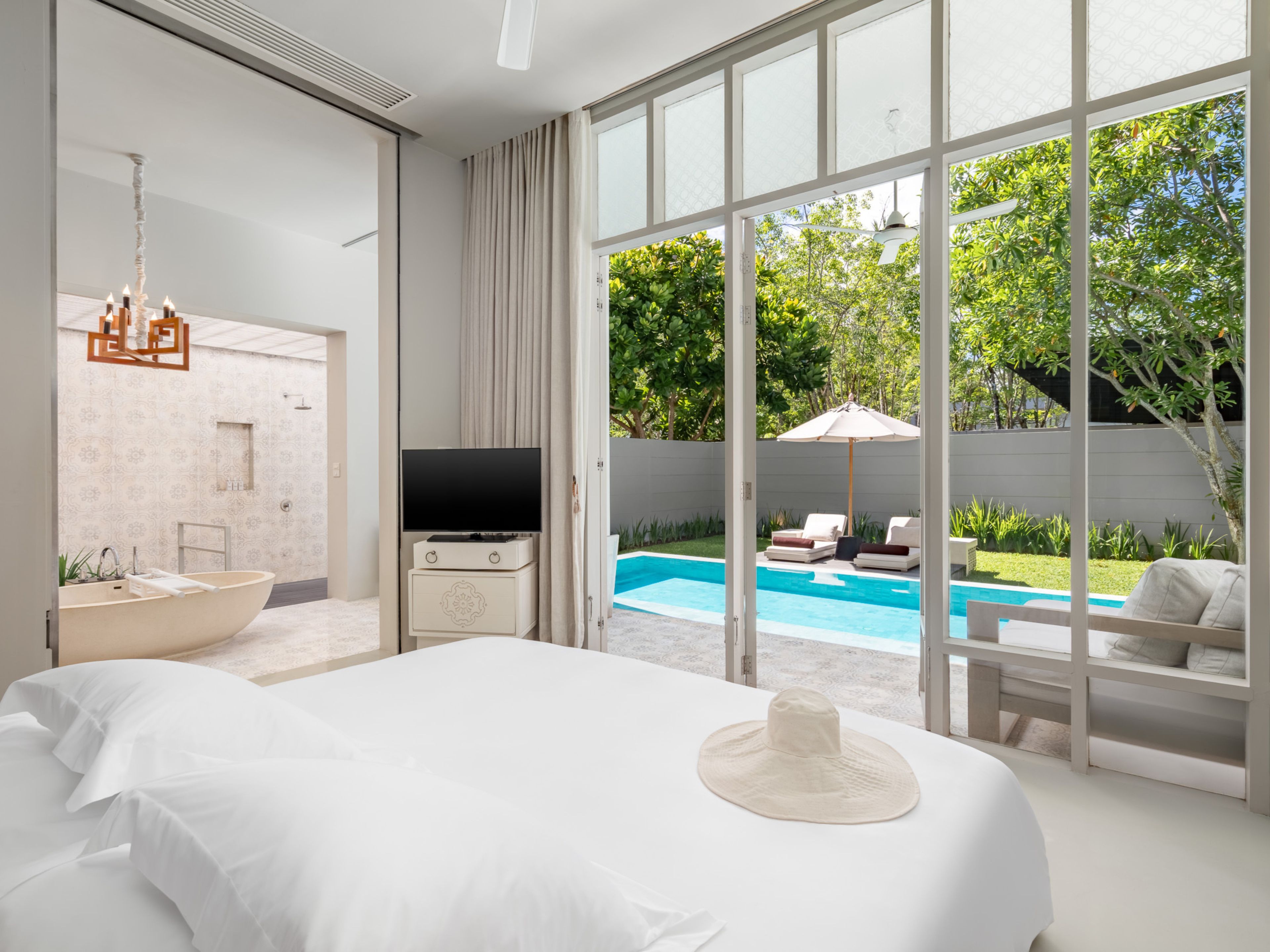 A modern hotel room with a large bed, a television, a bathtub, and a view of a swimming pool.