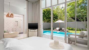 A modern hotel room with a large bed, a television, a bathtub, and a view of a swimming pool.