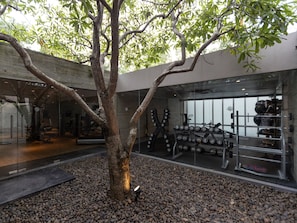A gym with exercise equipment, a tree, and a pebbled floor. - SALA Phuket Mai Khao Beach Resort (Mai Khao)