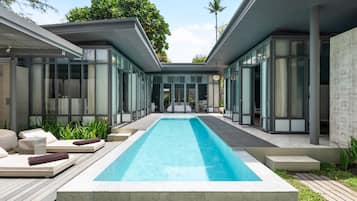 A modern pool area with a rectangular pool, lounge chairs, and a glass-enclosed building.