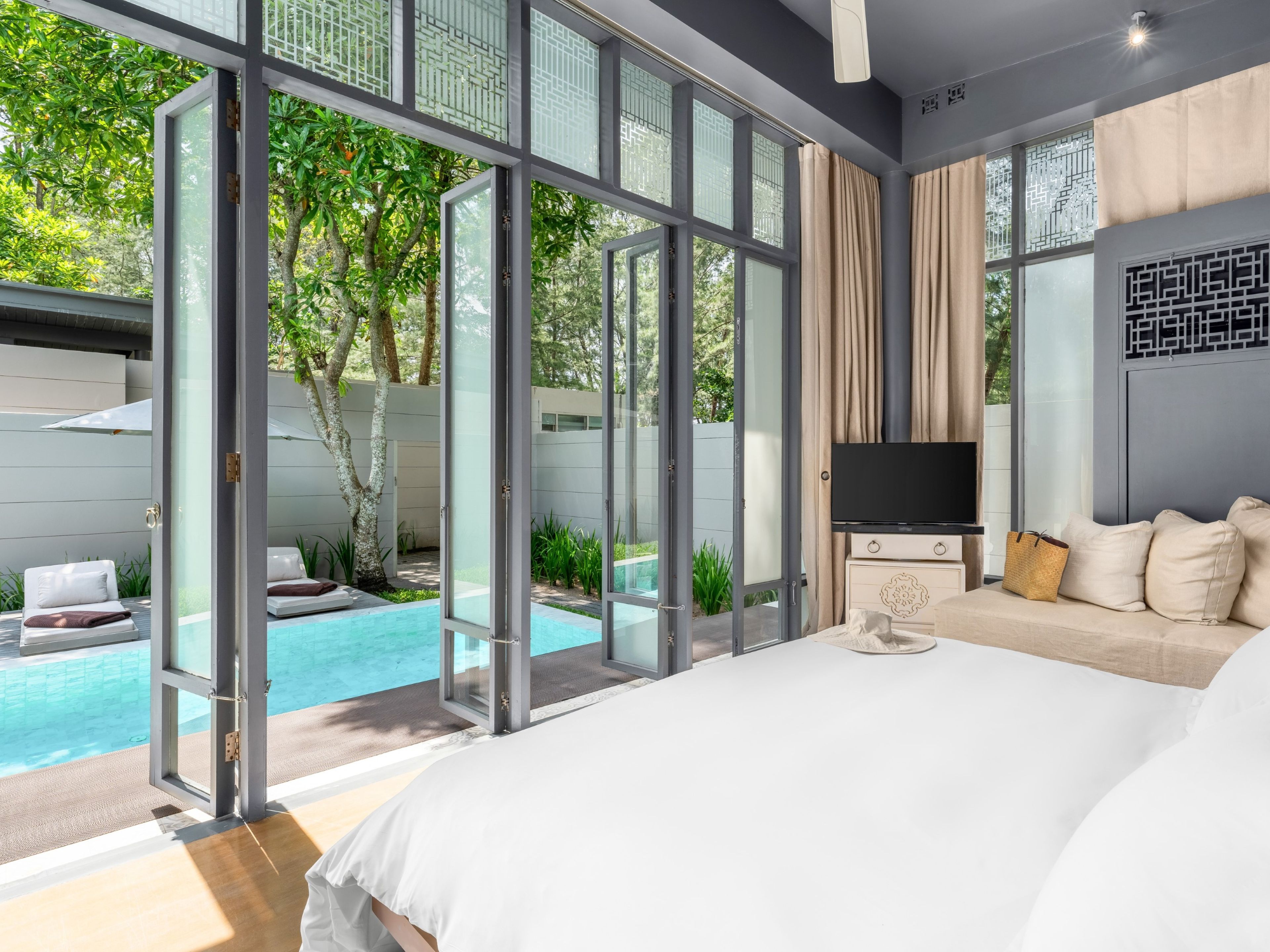 Un dormitorio moderno con una cama grande, un televisor y vistas a una piscina al aire libre.