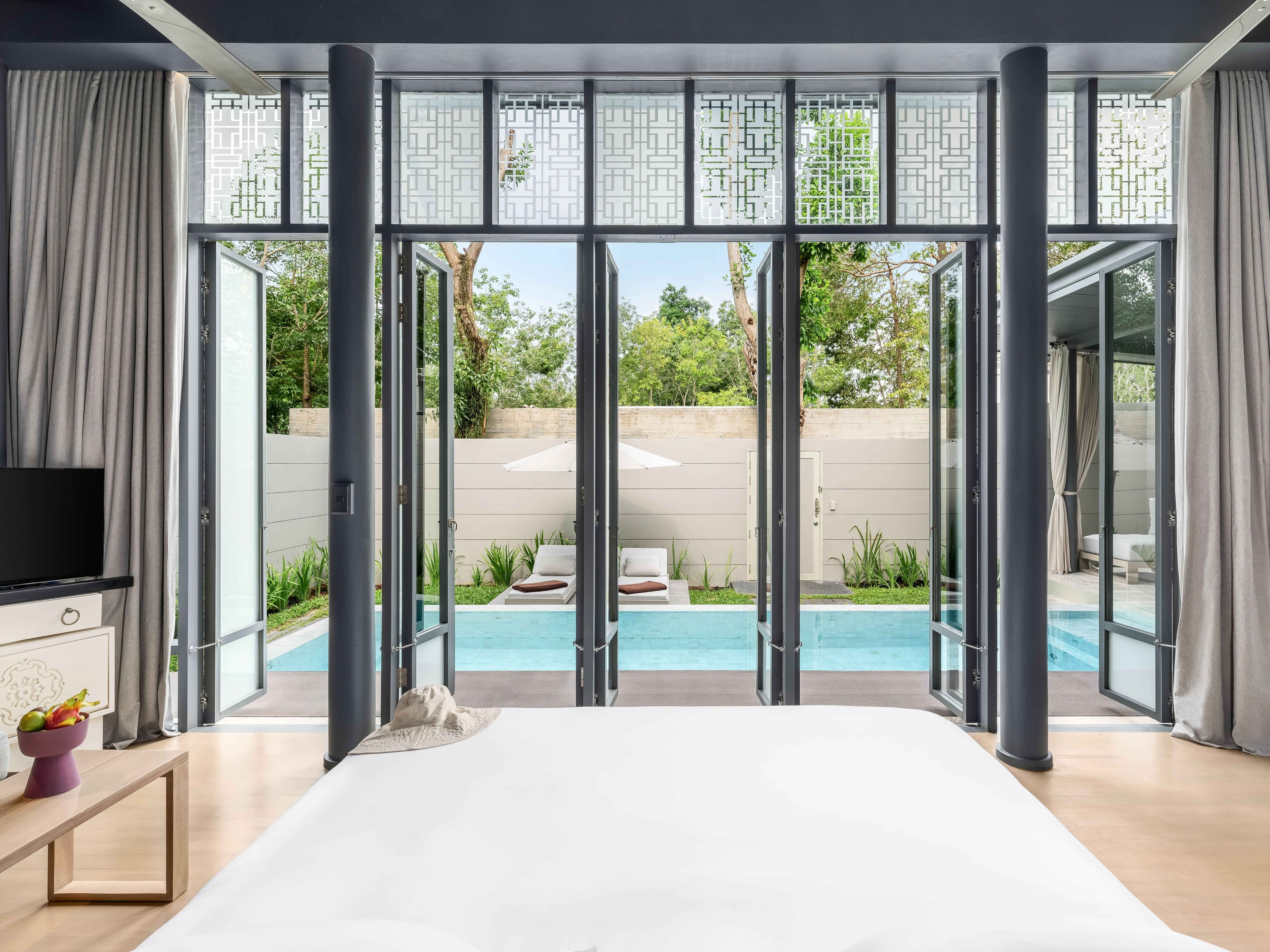 Un dormitorio moderno con una cama grande, un televisor y vistas a una piscina exterior a través de puertas de vidrio del suelo al techo.