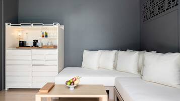 A modern living room with a white sofa, a wooden coffee table with fruit, and a white storage unit with kitchen appliances.