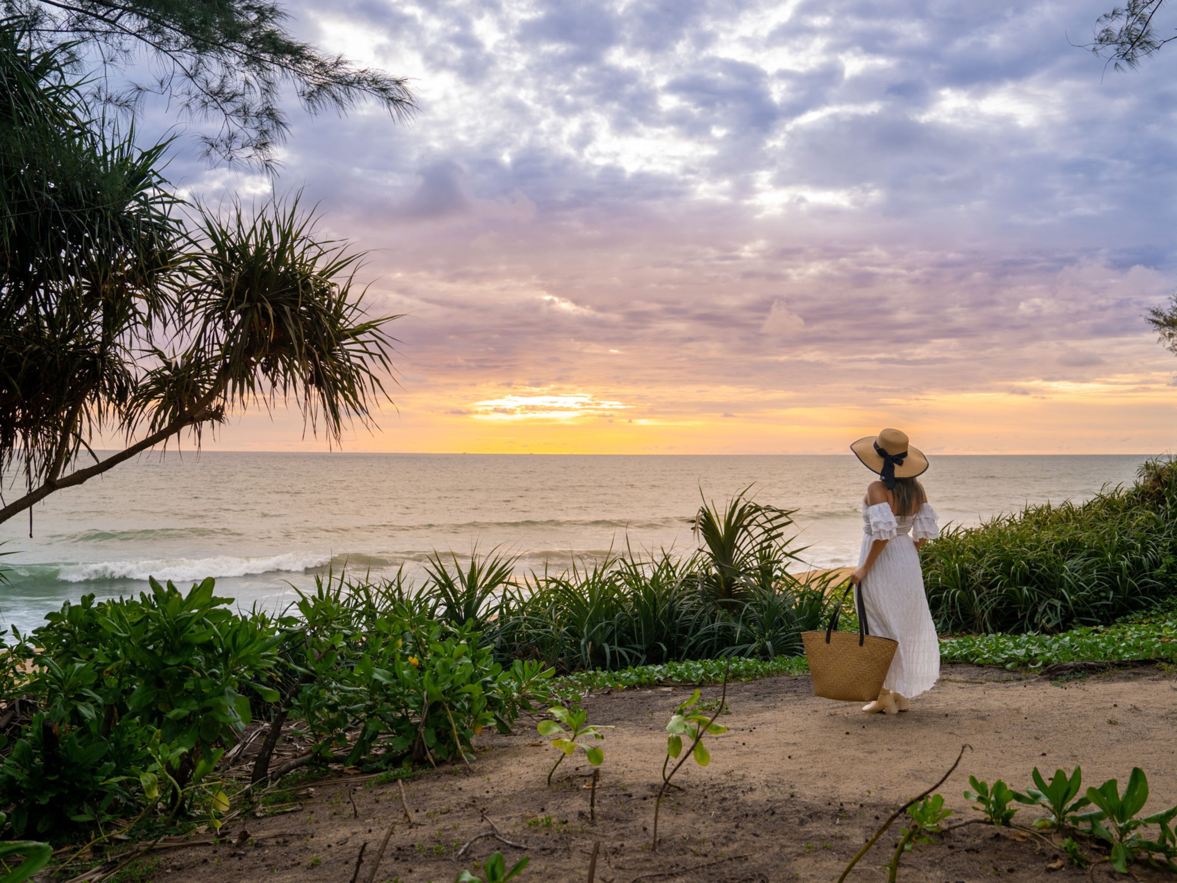 Una persona de pie en una playa arenosa, con vista al océano y al atardecer.