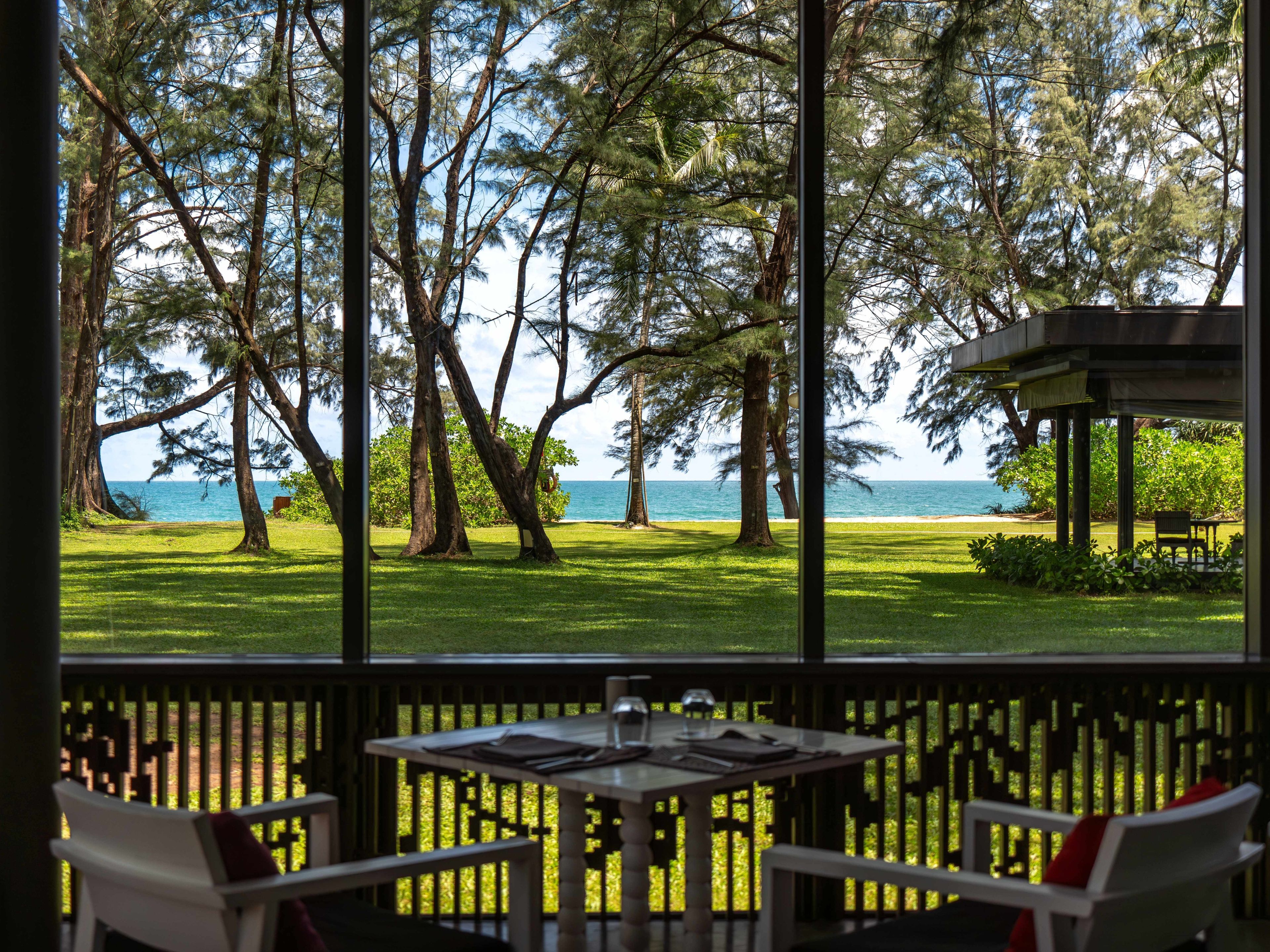 A view from a covered outdoor area with a table and chairs, overlooking a grassy area with trees and a body of water.