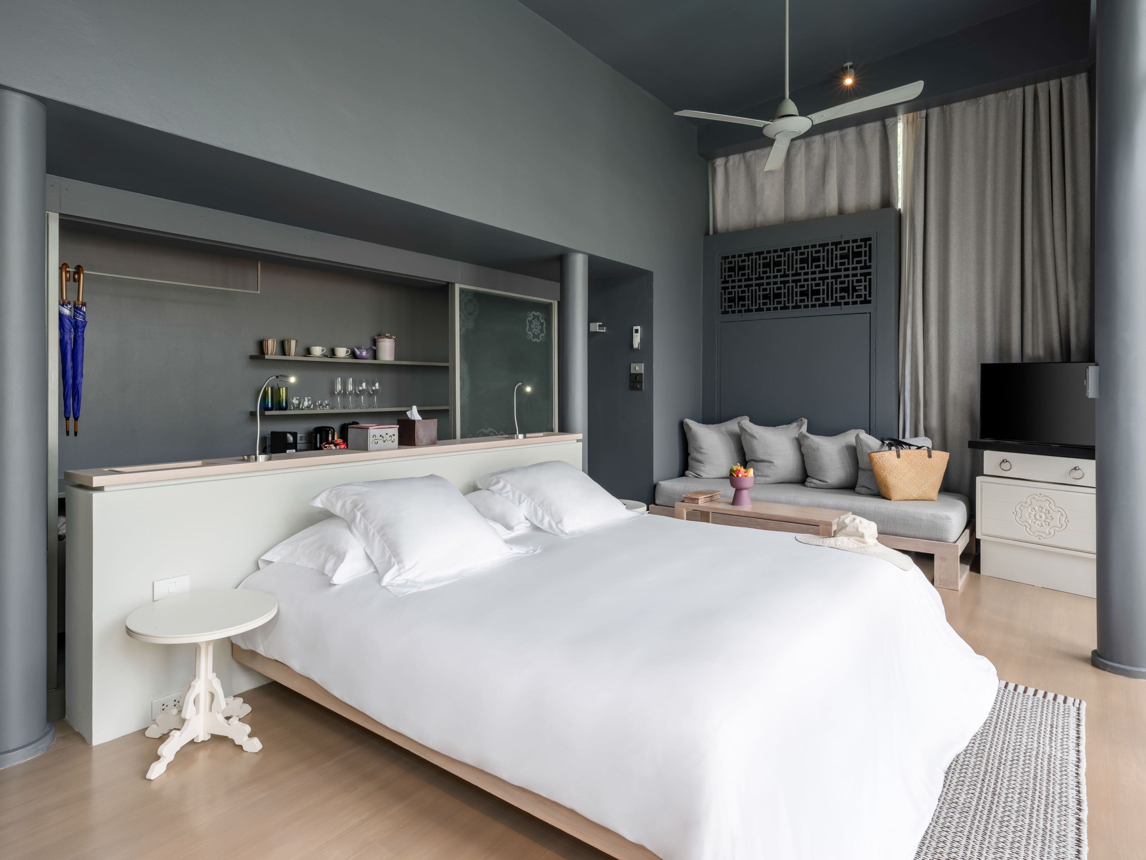 Una habitación de hotel moderna con una cama grande, una mesita pequeña, un sofá, un televisor y un ventilador de techo.