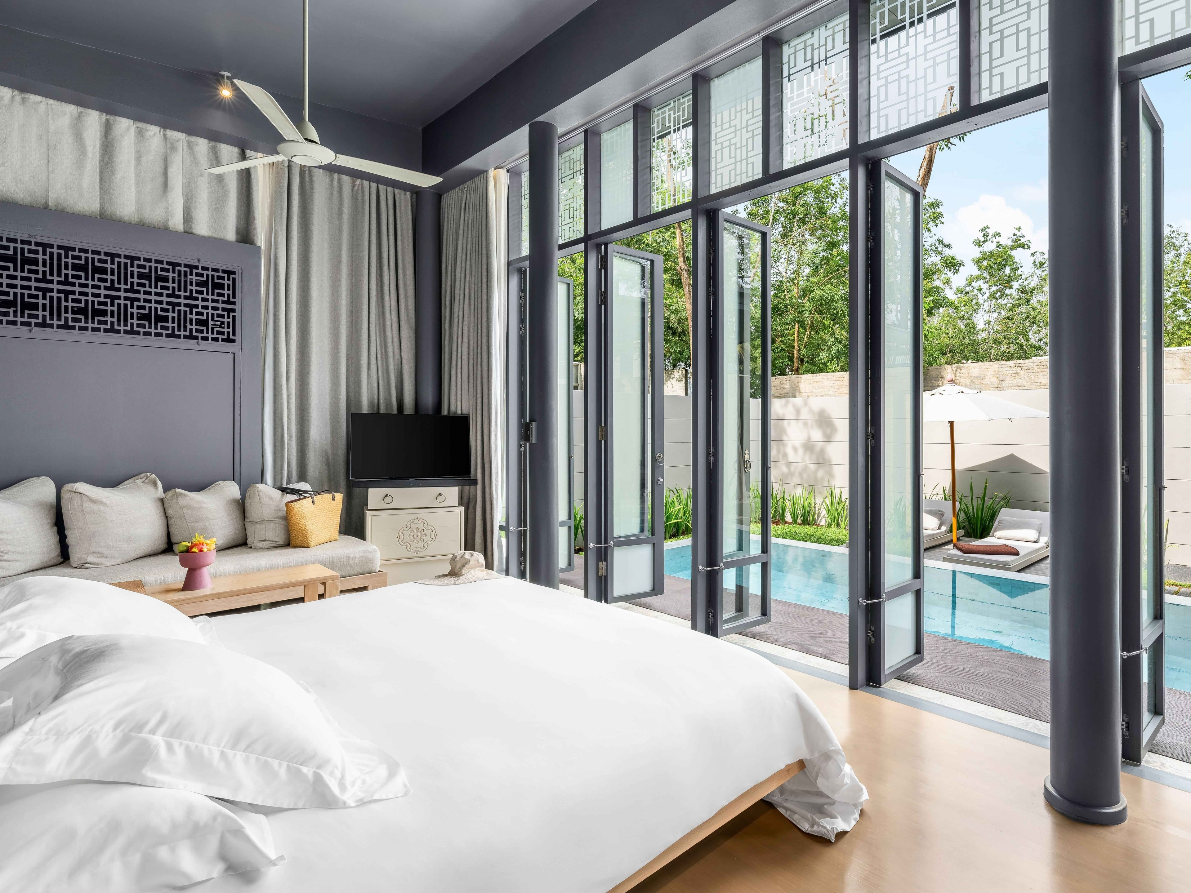 Un dormitorio moderno con una cama grande, un televisor de pantalla plana y vista a una piscina al aire libre.