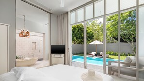 A modern hotel room with a large bed, a TV, a bathroom with a bathtub, and a view of a swimming pool and greenery. - SALA Phuket Mai Khao Beach Resort (Mai Khao)