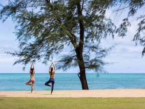Two individuals practicing yoga on a beach with a tree and ocean in the background. - SALA Phuket Mai Khao Beach Resort (Mai Khao)