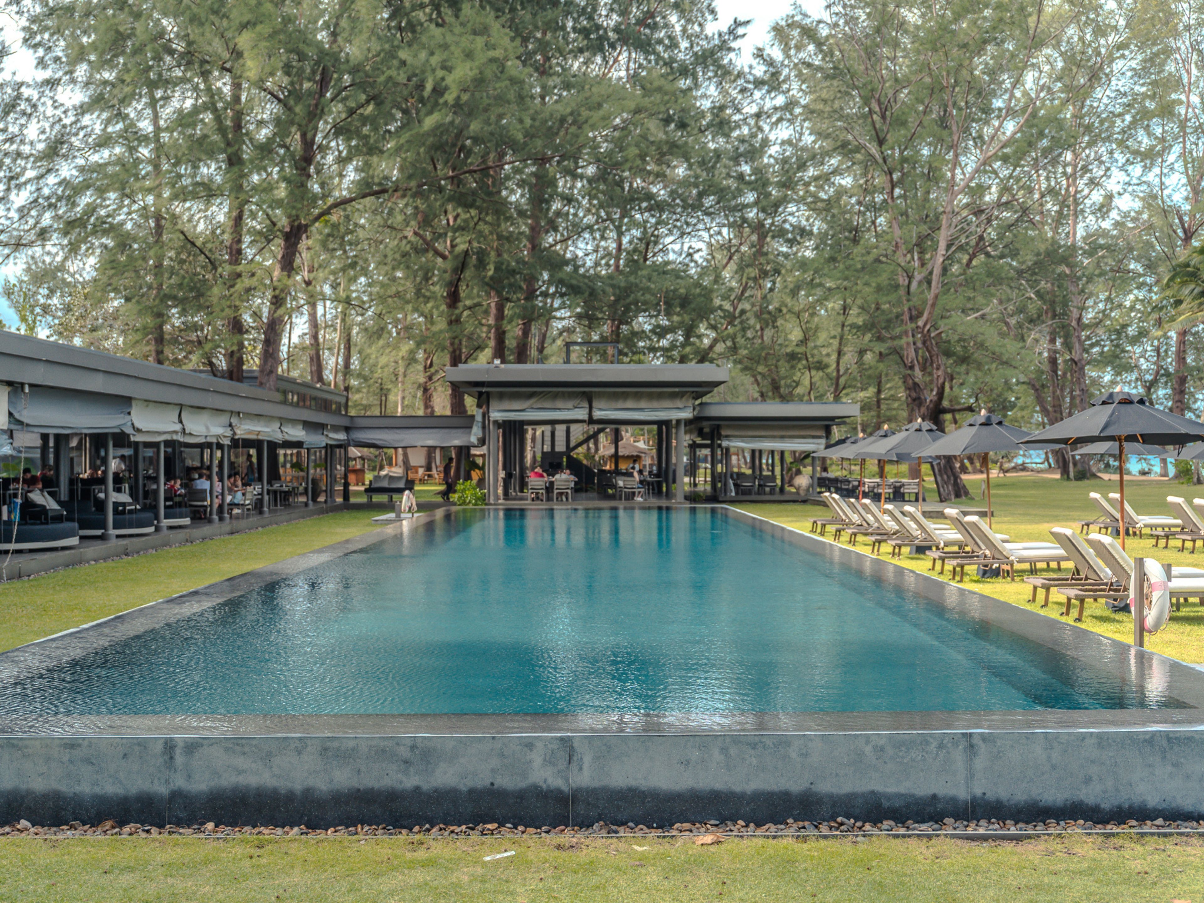A swimming pool with lounge chairs and shaded areas, surrounded by trees.