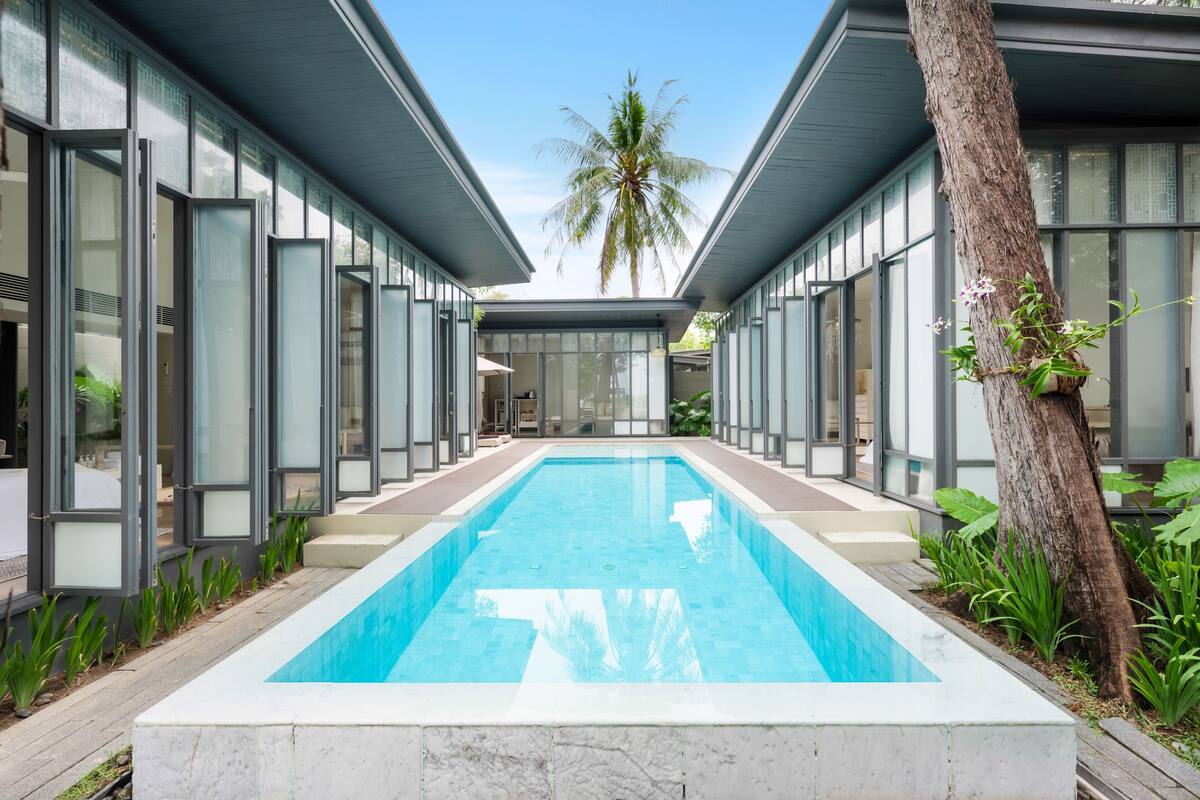 Ein modernes Gebäude mit einem zentralen Schwimmbecken, großen Glasfenstern und einer Palme.