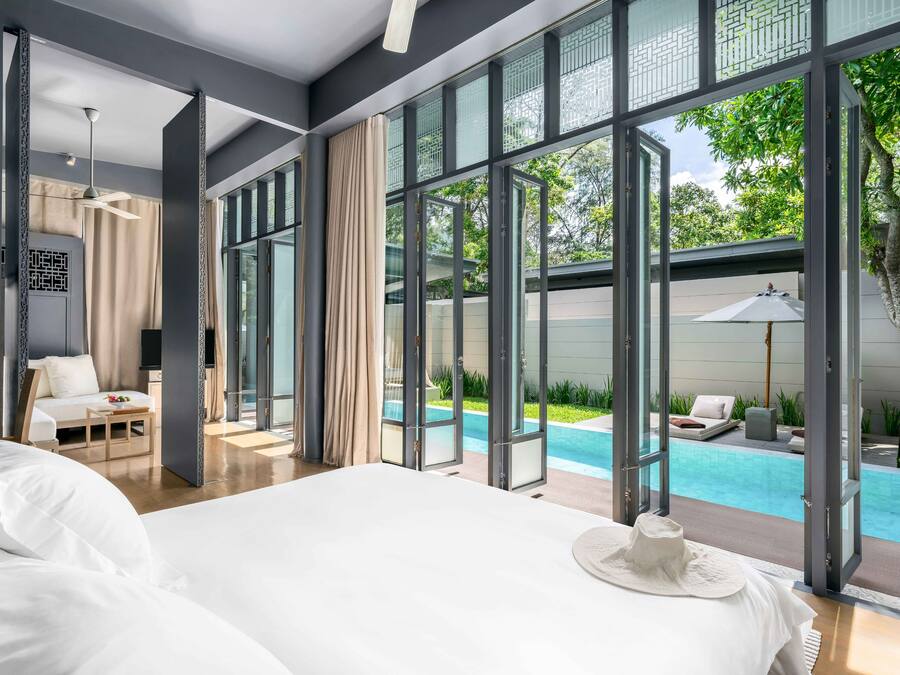 Habitación de hotel moderna con una cama grande, vista a una piscina al aire libre y un balcón con vista al verdor.